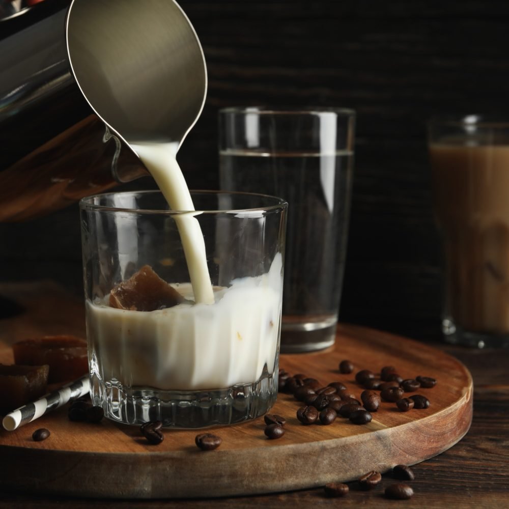 milk-is-poured-into-a-glass-of-coffee-composition-with-ice-coffee-e1625191305263
